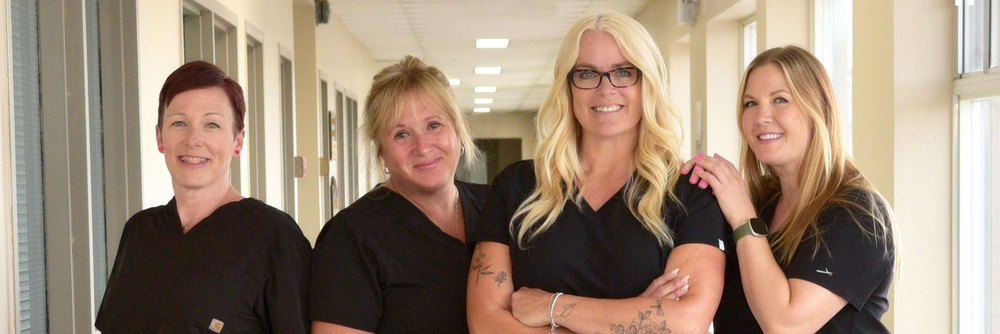 Four women in black uniforms standing together in a hallway.